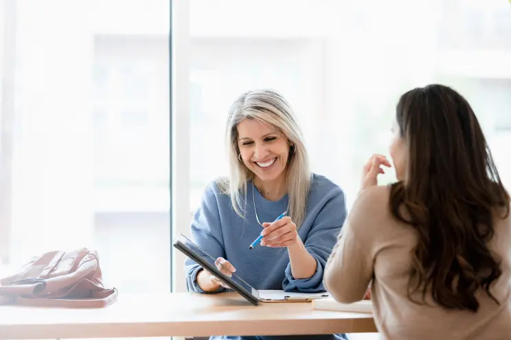 Woman with clipboard talking to another woman at a desk