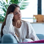 unhappy woman sitting on her couch thinking