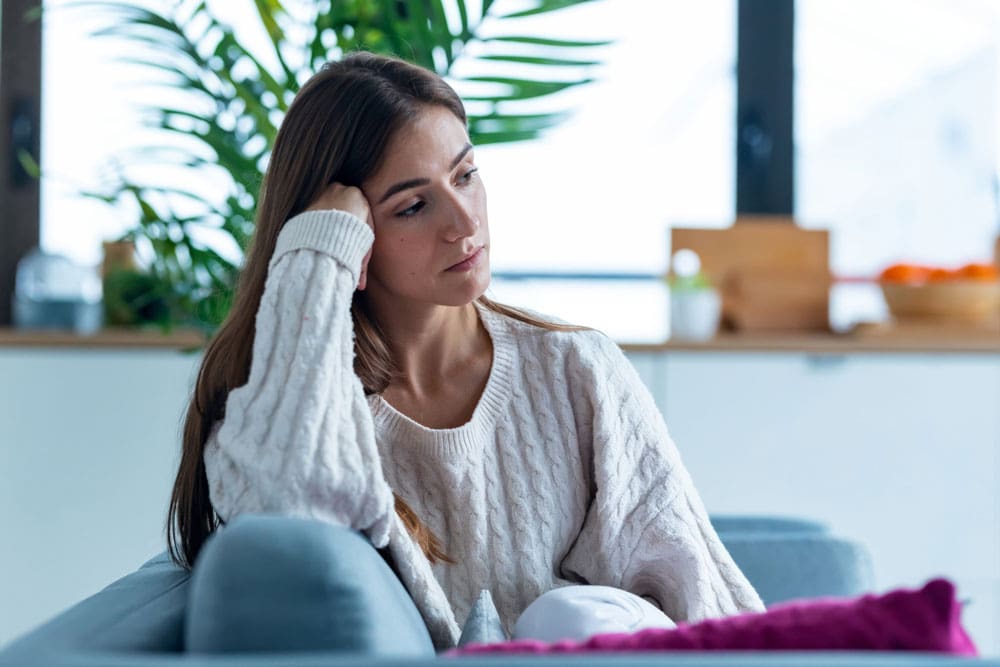 unhappy woman sitting on her couch thinking