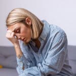 woman sitting on the couch looking worried with her head in her hand - anxiety - generalized anxiety disorder