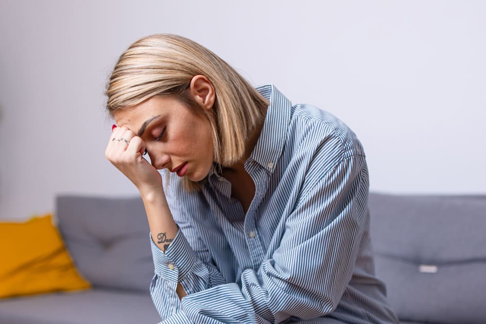 woman sitting on the couch looking worried with her head in her hand - anxiety - generalized anxiety disorder