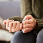 Close-up of a person sitting and holding their hands, with a focus on their sweater sleeves.