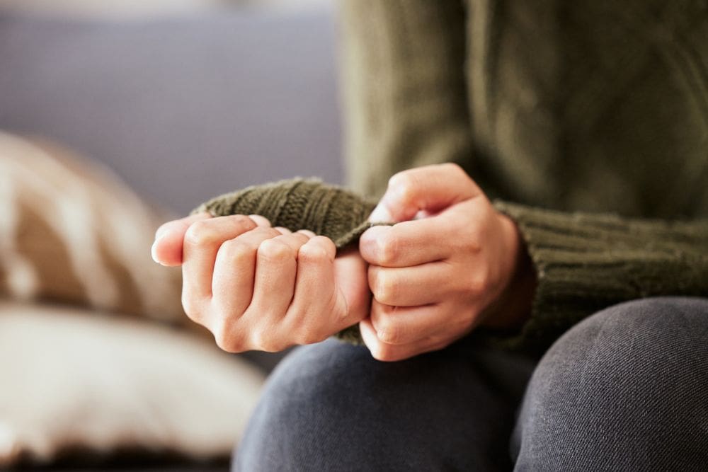 Close-up of a person sitting and holding their hands, with a focus on their sweater sleeves.