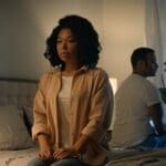 Raleigh Oaks - The Anxiety-Avoidance Cycle Understanding Why Your Anxiety Grows When You Avoid Things. A frustrated couple sits in a dimly lit bedroom. The woman faces away from the man as she looks upset and disgruntled.