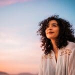 A woman with curly hair looks up with a bright smile, conveying a sense of optimism and cheerfulness.