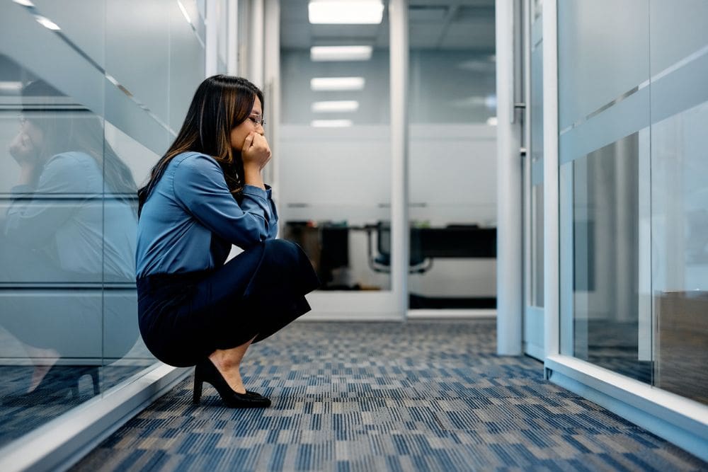 Raleigh Oaks - Coping With Bipolar Disorder at Work. A woman squats down with an axious look in her face in the hall of a professional office building